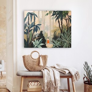 Puede incluir: Una impresi&oacute;n en lienzo cuadrada representa una exuberante escena de la jungla con una persona con un vestido naranja. Un bolso tote de paja tejida con un asa circular y una borla blanca descansa sobre un banco gris. Una manta con flecos y cajas decorativas completan la escena.