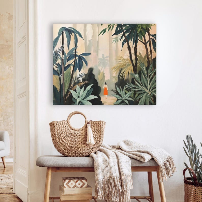 Puede incluir: Una impresi&oacute;n en lienzo cuadrada representa una exuberante escena de la jungla con una persona con un vestido naranja. Un bolso tote de paja tejida con un asa circular y una borla blanca descansa sobre un banco gris. Una manta con flecos y cajas decorativas completan la escena.