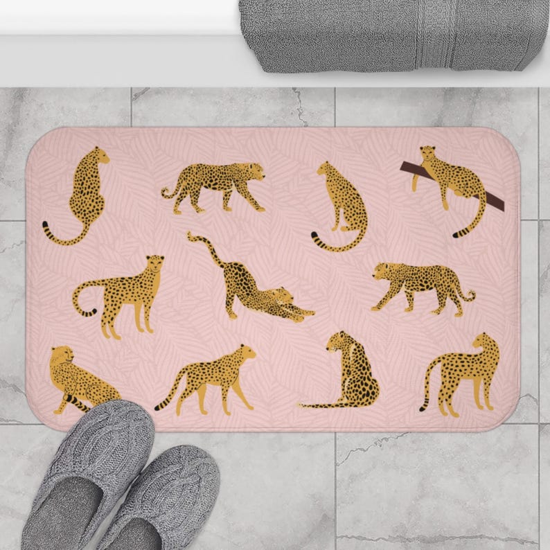 May include: A pink bath mat with a repeating pattern of cheetah print. The cheetah print is in shades of brown and yellow. The mat is rectangular and has a textured surface.