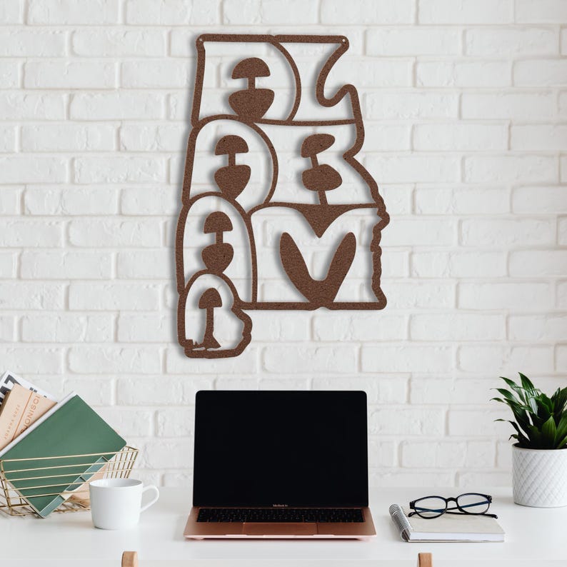 Puede incluir: Una pieza de arte mural de metal marr&oacute;n que deletrea la palabra "DREAM" en una fuente estilizada. La obra de arte est&aacute; montada en una pared de ladrillo blanco. Una computadora port&aacute;til, una taza de caf&eacute; y otros suministros de oficina est&aacute;n en un escritorio blanco debajo.