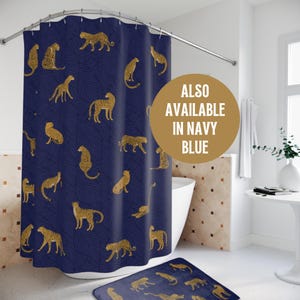 May include: A navy blue shower curtain with a gold leopard print pattern. The shower curtain is hanging on a curved shower rod. The text "ALSO AVAILABLE IN NAVY BLUE" is on a gold circle in the upper right corner of the image.