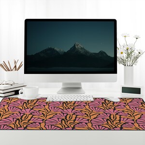May include: A desk with a computer monitor, keyboard, mouse, and a cup of coffee. The desk has a patterned desk mat with pink and orange flowers on a black background.