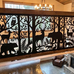 May include: Black metal railing featuring a forest scene cut-out design. Silhouettes of trees, deer, bears, owls, squirrels, and other wildlife are featured. The railing is framed by wooden beams, creating a rustic aesthetic.