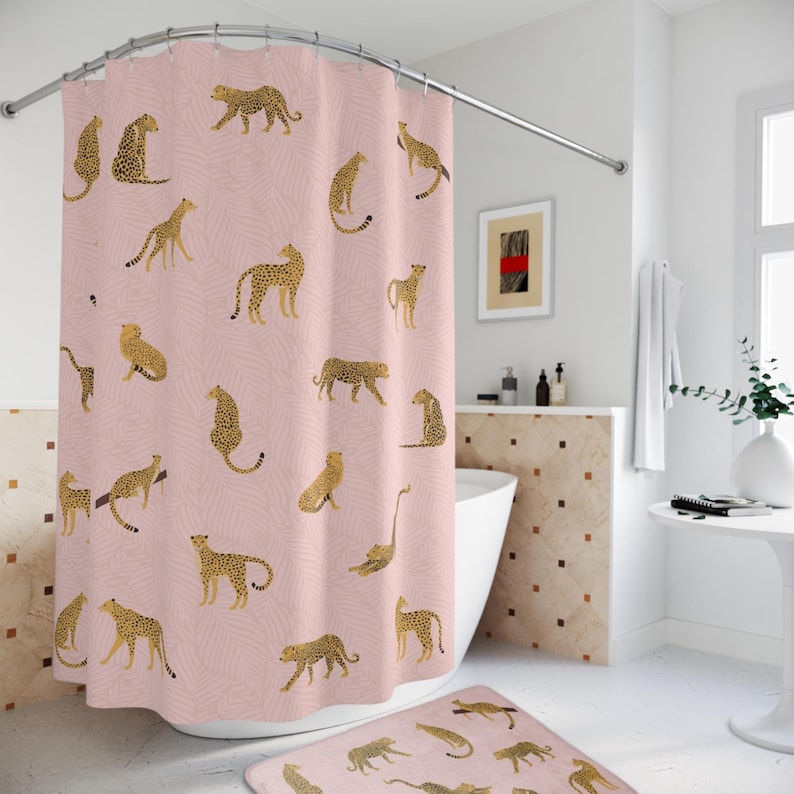 May include: A pink shower curtain with a repeating pattern of gold leopards. The shower curtain is hung on a curved shower rod. A matching pink bath mat with gold leopards is on the floor.