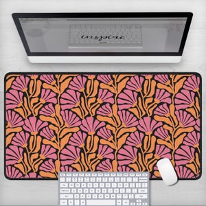 May include: A black desk mat with a floral pattern featuring pink and orange flowers on a black background. The mat is designed to protect your desk surface and provide a smooth surface for your mouse.