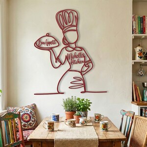 Deep red metal female chef wall art with personalized "Michelle's Kitchen" text hanging in a colorful, eclectic, rustic dining room with wooden table.