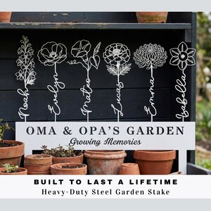 K&ouml;nnte beinhalten: Wei&szlig;e Gartenstecker aus Metall mit Blumendesigns und Namen: Noah, Evelyn, Mateo, Lucas, Emma und Isabella. Ein Schild lautet: &bdquo;OMA & OPA'S GARDEN Growing Memories&ldquo;. Der Text &bdquo;BUILT TO LAST A LIFETIME Heavy-Duty Steel Garden Stake&ldquo; ist ebenfalls sichtbar.