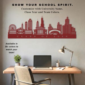May include: A red metal wall art piece showing a city skyline, with the text "CLASS OF 2026". The text "SHOW YOUR SCHOOL SPIRIT" and "Customize with University Name, Class Year and Team Colors" are also visible. The art is displayed above a desk.