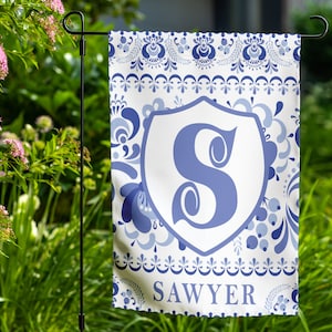 May include: A white garden flag with a blue and white floral pattern. A blue letter "S" is in a white shield in the center of the flag. The text "SAWYER" is at the bottom of the flag.