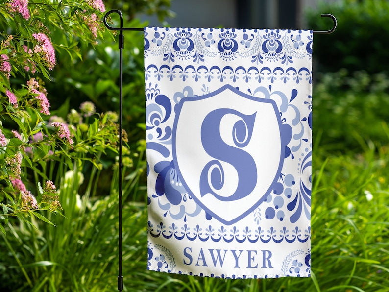 May include: A white garden flag with a blue and white floral pattern. A blue letter "S" is in a white shield in the center of the flag. The text "SAWYER" is at the bottom of the flag.