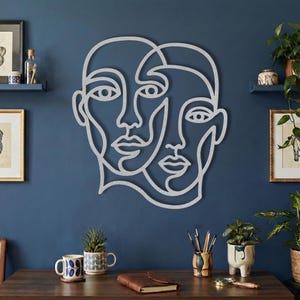Silver wire wall art, abstract face sign on blue wall.