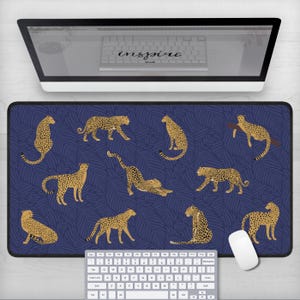 May include: A blue and gold cheetah print mousepad with a repeating pattern of cheetahs and palm leaves. The mousepad is on a white desk with a keyboard and a white computer mouse.