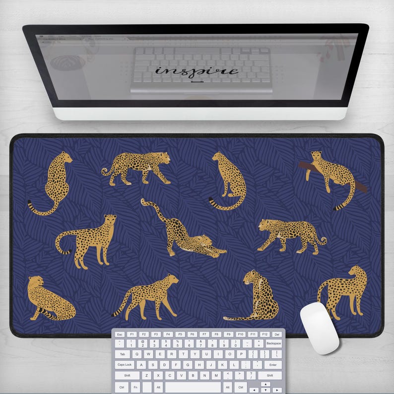 May include: A blue and gold cheetah print mousepad with a repeating pattern of cheetahs and palm leaves. The mousepad is on a white desk with a keyboard and a white computer mouse.