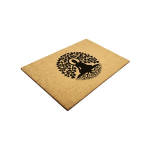 May include: A brown coir doormat with a black silhouette of a meditating figure sitting inside a tree with roots.