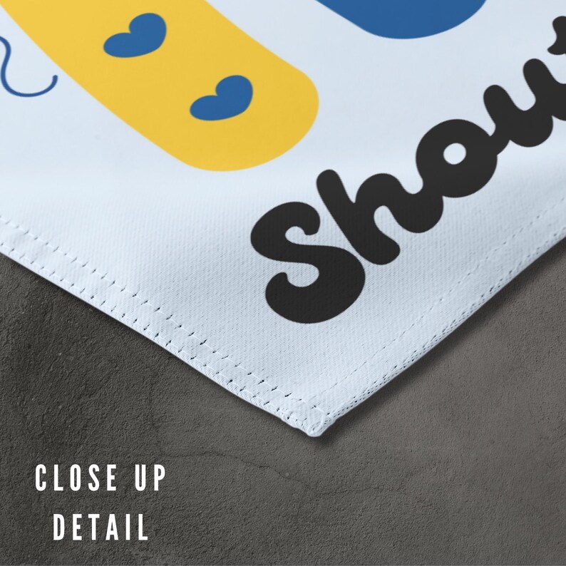 K&ouml;nnte beinhalten: Ein wei&szlig;es Stoffbanner mit blauen und gelben Formen und dem Text "Baby Shower" in Schwarz.