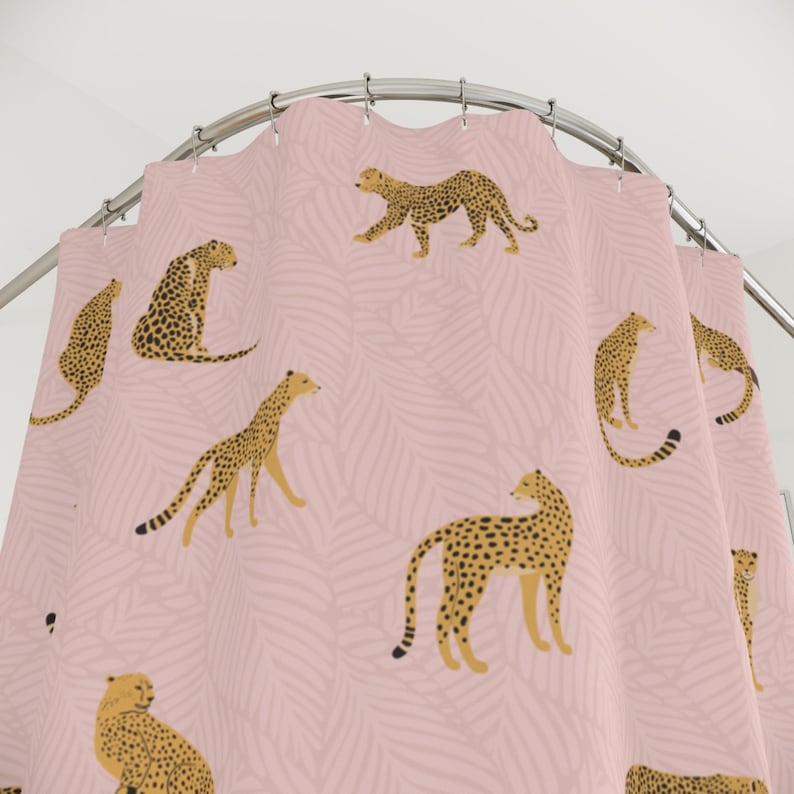 May include: Pink shower curtain with a repeating pattern of brown and black cheetahs on a pink background with a leaf pattern.