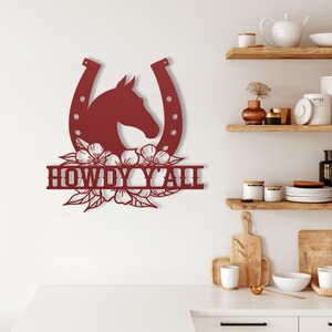 May include: A burgundy metal wall art piece featuring a horse head within a horseshoe, with floral accents and the text "HOWDY Y'ALL". The artwork is mounted on a white wall, suggesting a rustic or country theme.