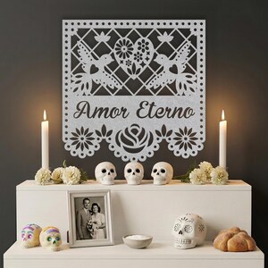 Op de afbeelding: Een altaar voor de Dag van de Doden met een decoratieve papieren uitsnede met de tekst "Amor Eterno". Het altaar bevat kaarsen, suikerschedels, een ingelijste foto, bloemen en een brood.