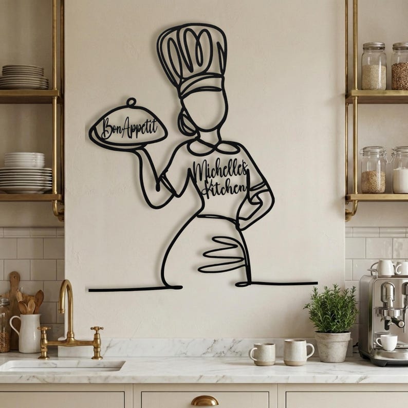 Black personalized metal kitchen sign reading "Michelle's Kitchen" mounted on a beige wall above a farmhouse sink and gold faucet.