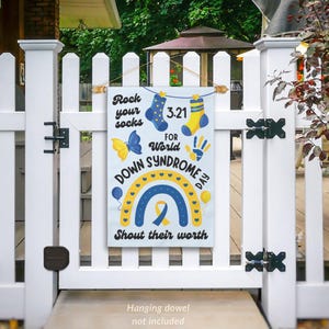 K&ouml;nnte beinhalten: Eine wei&szlig;e Gartenflagge mit einem blauen und gelben Regenbogen, einem gelben Schmetterling und dem Text "Rock your socks 3.21 for World Down Syndrome Day Shout their worth".