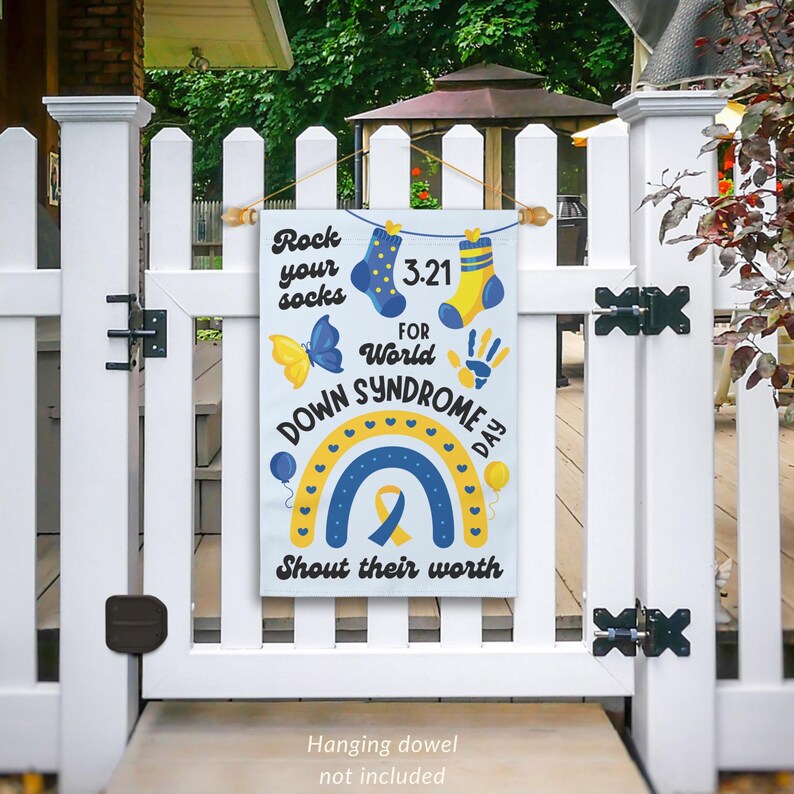 K&ouml;nnte beinhalten: Eine wei&szlig;e Gartenflagge mit einem blauen und gelben Regenbogen, einem gelben Schmetterling und dem Text "Rock your socks 3.21 for World Down Syndrome Day Shout their worth".