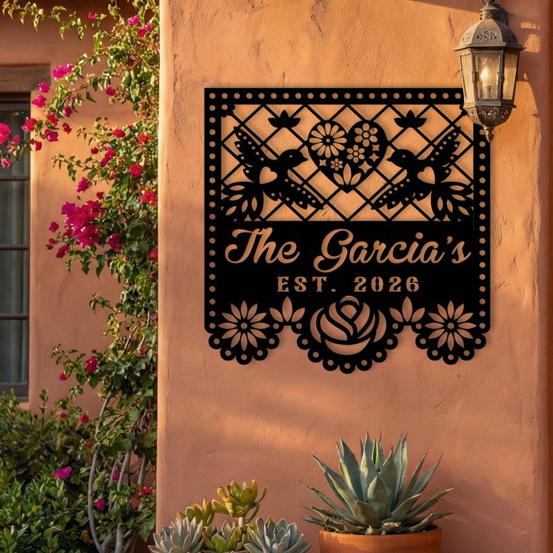 Op de afbeelding: Zwart metalen familienaambord met een decoratief ontwerp met kolibries, harten en bloemmotieven. Het bord leest "The Garcia's EST. 2026" en is geschikt voor buitengebruik.