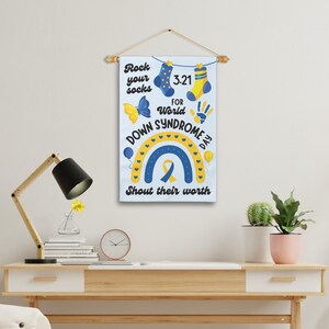 K&ouml;nnte beinhalten: Ein wei&szlig;es Banner mit einem Regenbogen, gelben und blauen Socken, einem Schmetterling, einem Handabdruck und dem Text "Rock your socks 3-21 for World Down Syndrome Day Shout their worth".