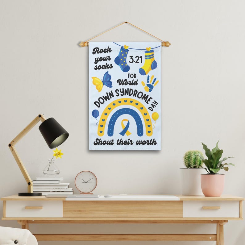 K&ouml;nnte beinhalten: Ein wei&szlig;es Banner mit einem Regenbogen, gelben und blauen Socken, einem Schmetterling, einem Handabdruck und dem Text "Rock your socks 3-21 for World Down Syndrome Day Shout their worth".