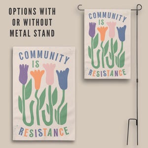 May include: A garden flag with a white background and colourful tulips. The text "COMMUNITY IS RESISTANCE" is printed in a colourful font.