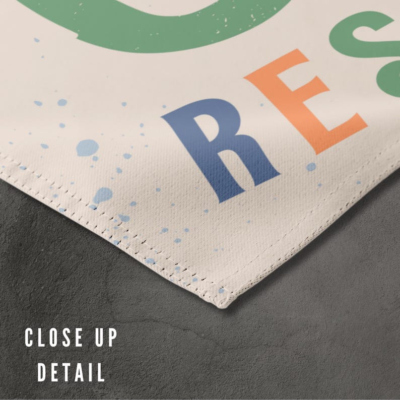 May include: Close-up detail of a white canvas with a stitched edge. The canvas has a blue, orange, and green design with the word "REST" printed in large letters.