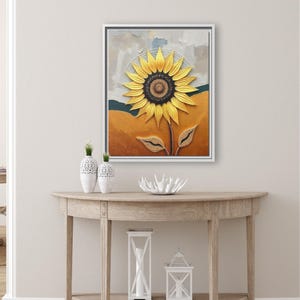 Puede incluir: Una obra de arte enmarcada que presenta un gran girasol amarillo con un centro marr&oacute;n oscuro. La pintura tiene una apariencia texturizada, con un fondo de tonos naranja, azul y gris. La obra de arte se exhibe sobre una consola de madera.