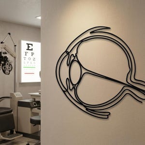 Minimalist black metal eyeball sculpture mounted in an optometry exam room next to vision testing equipment.