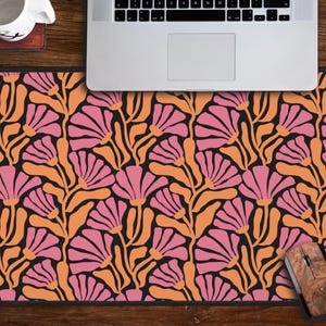 May include: A pink and orange floral patterned mouse mat with a black background. The mouse mat is on a wooden desk with a laptop and a mouse.