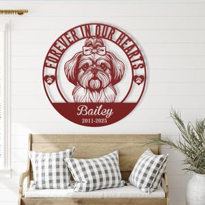 Puede incluir: Una pieza de arte mural de metal burdeos con un dise&ntilde;o de perro Shih Tzu. El marco circular dice "Forever in Our Hearts" e incluye el nombre "Bailey" y las fechas "2011-2025". Huellas de patas y un lazo acent&uacute;an el dise&ntilde;o.