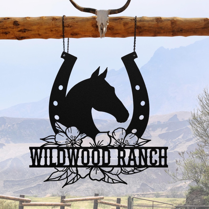 May include: Black metal Wildwood Ranch sign featuring a horse head silhouette inside a horseshoe, adorned with floral accents. The sign is suspended by chains from a wooden beam, with a skull and horns above.