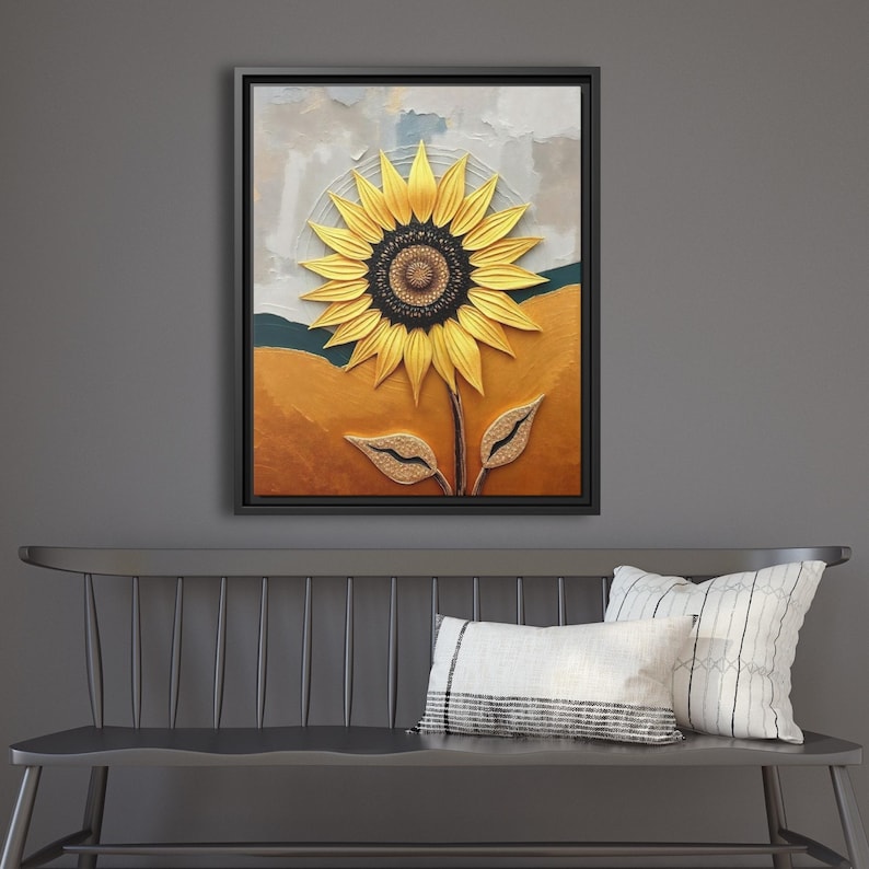 Puede incluir: Una obra de arte enmarcada con un girasol texturizado. El girasol tiene p&eacute;talos amarillos y un centro marr&oacute;n oscuro. El fondo incluye tonos de oro, verde azulado y gris, con un marco negro. La obra de arte se exhibe sobre un banco gris.