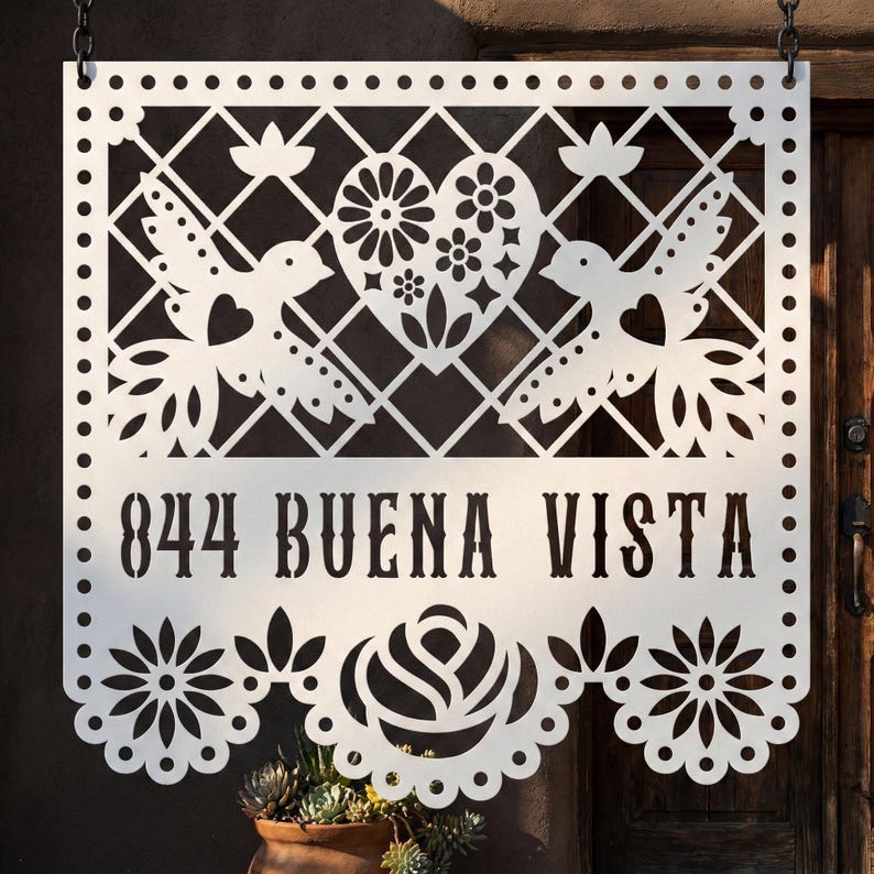 Op de afbeelding: Wit metalen bord met een decoratief uitgesneden ontwerp. Het bord toont het adres "844 BUENA VISTA" in vette letters, samen met duiven, bloemen en een hart. Het bord hangt aan een ketting.