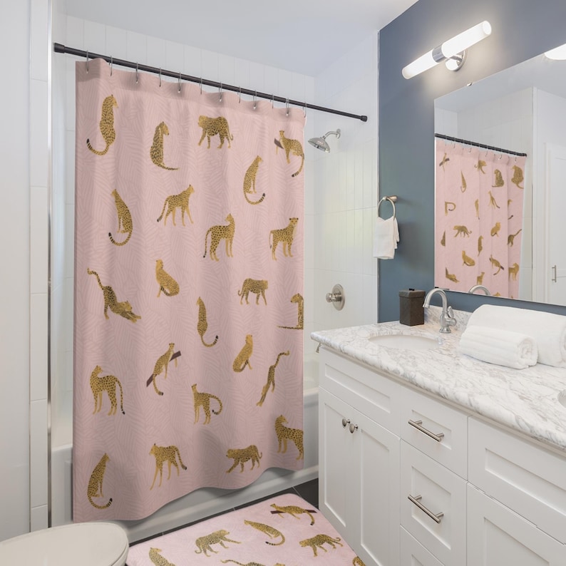 May include: A pink shower curtain with a pattern of gold leopards. The shower curtain is in a bathroom with a white vanity and a white toilet.