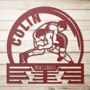 Op de afbeelding: Een rood metalen bord met twee worstelaars in actie, geplaatst in een cirkelvormig frame. De naam "COLIN" staat in een boog bovenaan, met "BULLDOGS" en een gestileerd ontwerp eronder. Ontworpen voor wandmontage.