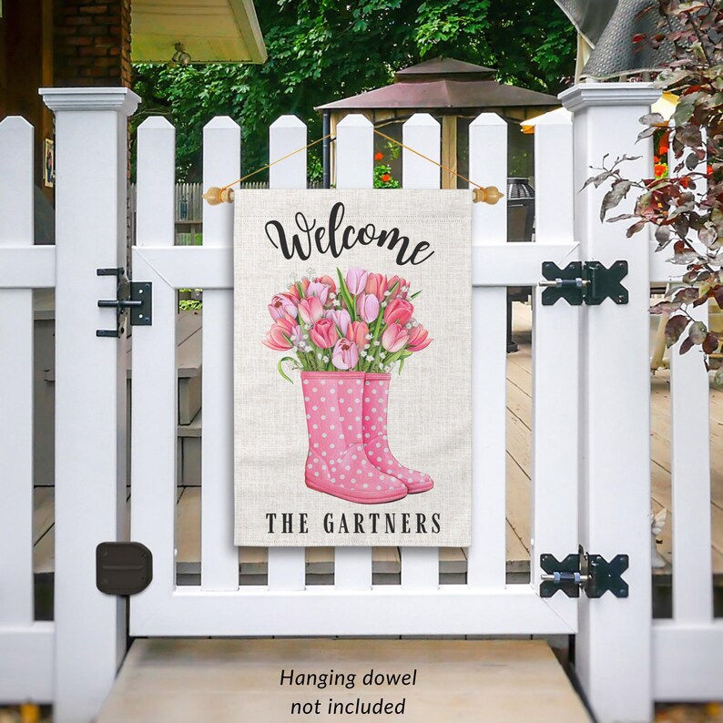 May include: A welcome garden flag with a pink and white floral design in pink rain boots. The text "Welcome" and "The Gartners" is printed on the flag.