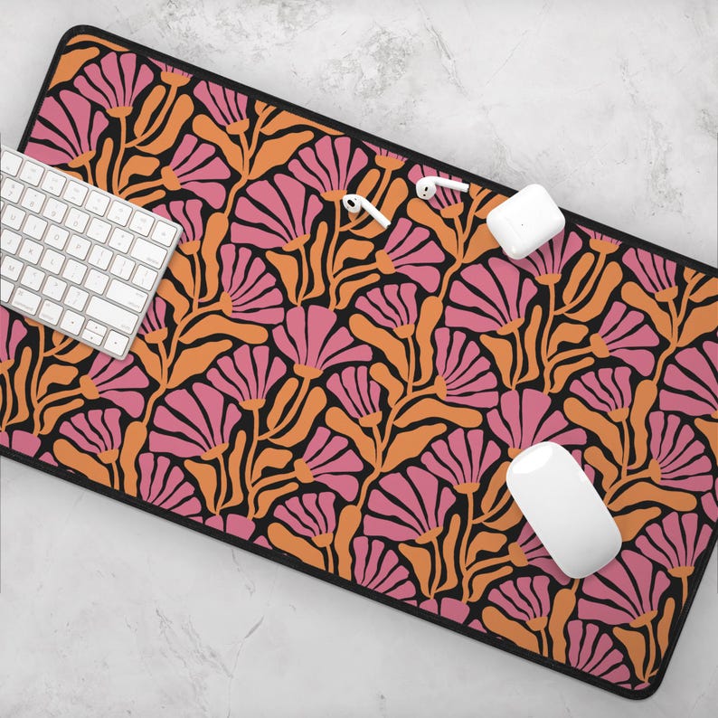May include: A black desk mat with a repeating pattern of pink and orange stylised flowers on a black background. The mat is designed to protect a desk surface from scratches and wear.