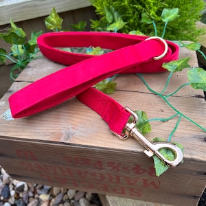 May include: Red velvet dog leash with a gold metal clip and a gold metal ring. The leash is on a wooden surface.