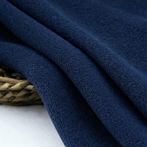 May include: Close-up of a navy blue fleece fabric. The fabric is soft and textured, with a slightly uneven surface. The folds and shadows create depth and dimension, highlighting the plush texture of the material. The fabric is likely used for clothing or blankets.