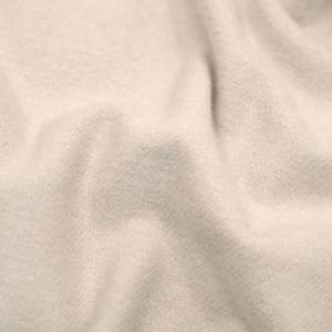 Puede incluir: Primer plano de una tela color crema con una sutil textura tejida. La tela es suave y parece estar drapeada, con pliegues y sombras suaves que crean profundidad. El color neutro y la textura sugieren un textil acogedor, posiblemente para una manta o bufanda.
