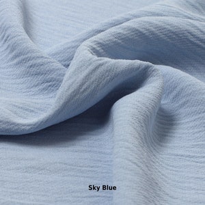 May include: A close-up of a soft, textured fabric in a light blue color. The fabric is folded and draped, showcasing its texture and drape. The text "Sky Blue" is visible at the bottom of the image.