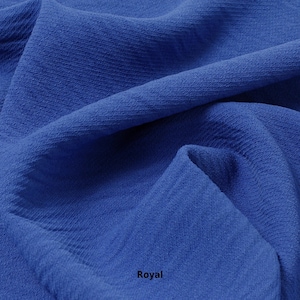 May include: Close-up of a royal blue fabric with a textured surface. The fabric is folded and draped, showing its soft and flowing texture.