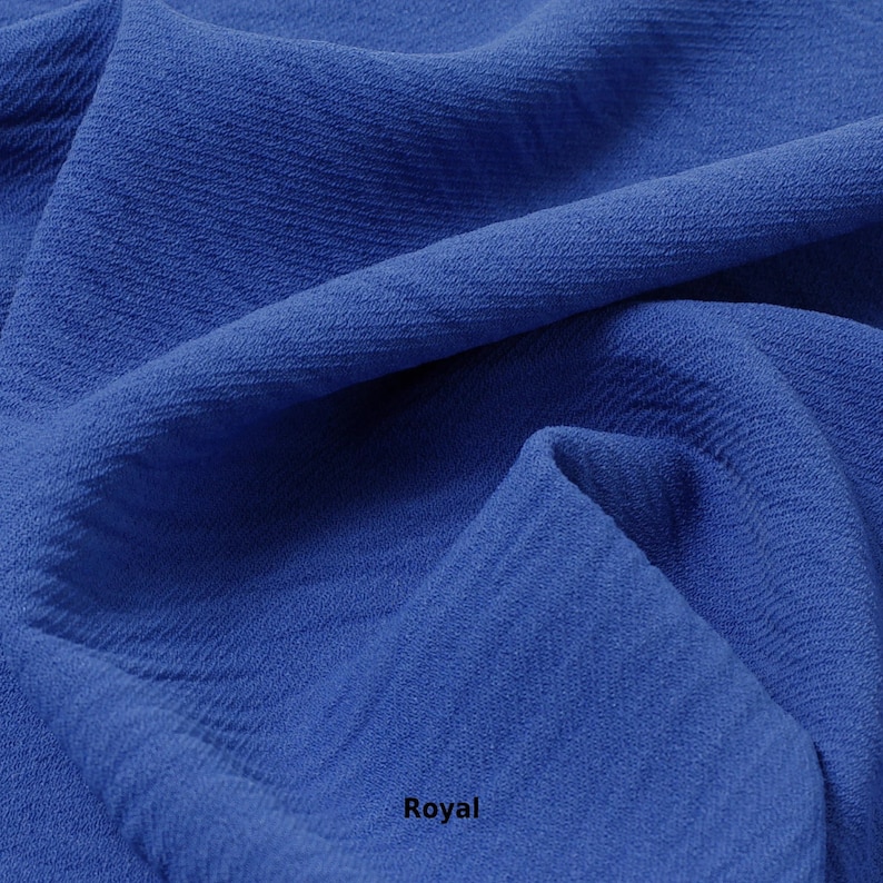 May include: Close-up of a royal blue fabric with a textured surface. The fabric is folded and draped, showing its soft and flowing texture.