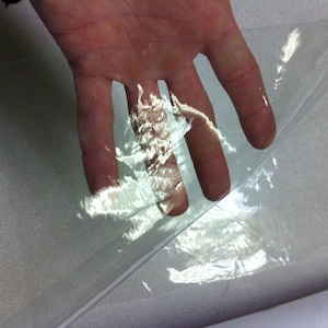 May include: A clear plastic sheet is being held up by a hand. The sheet is translucent and has a slight ripple effect.