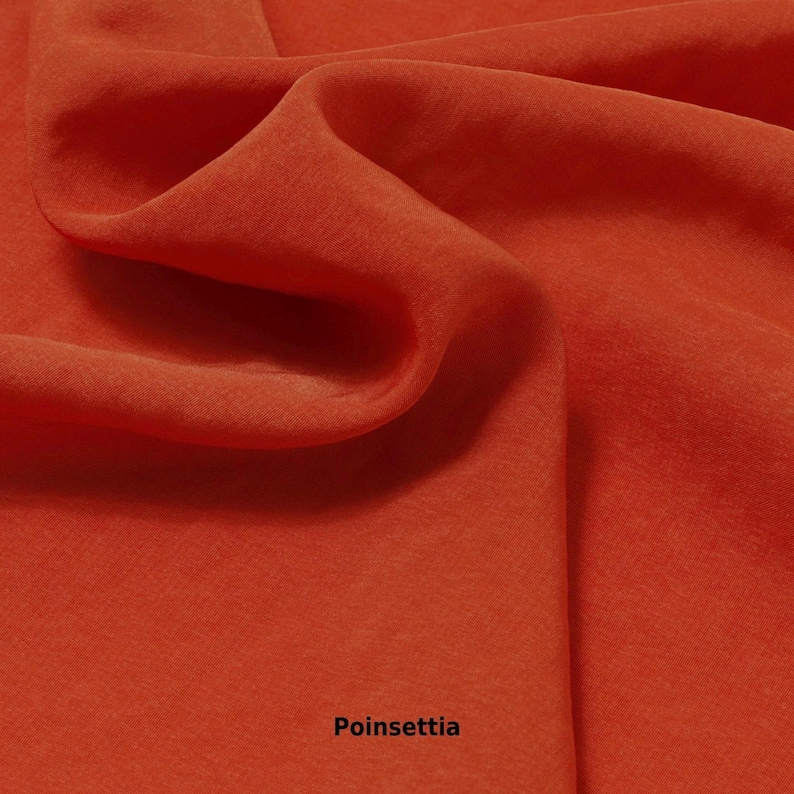 May include: Close-up of a flowing, textured fabric in a vibrant poinsettia red color. The fabric is draped, creating soft folds and shadows. The word "Poinsettia" is printed at the bottom of the image.
