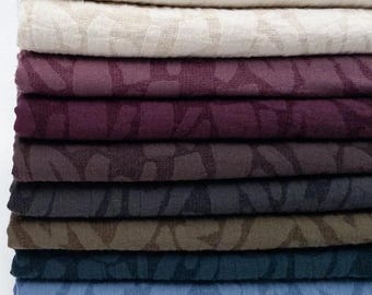 Puede incluir: Una pila de piezas de tela dobladas en varios colores, incluyendo blanco, crema, ciruela, morado oscuro, marrón, carbón, oliva, cerceta, azul claro y negro. Cada pieza de tela presenta un patrón de hojas tonal consistente y repetitivo.